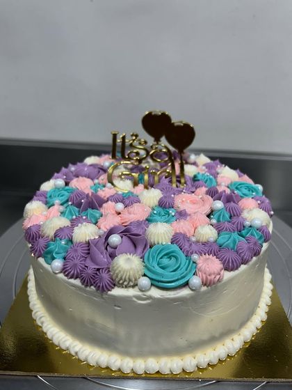 A beautiful cake to welcome a cute soul into the world. This "It's a Girl!" cake is covered in a vibrant floral arrangement of buttercream swirls in purple, pink, and teal.