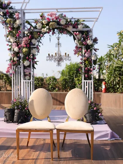 The bride and groom's seating at the mandap for Reeya and Parth's wedding. The chairs are framed by a beautiful floral arch and a hanging crystal chandelier, creating a picture-perfect setting.