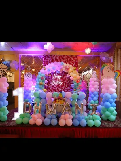 A large stage setup for a unicorn-themed first birthday, featuring balloon pillars, a sequin backdrop, and marquee letters spelling out the name.