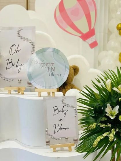 We provide a full suite of themed stationery. This display features mini easels with 'Oh Baby' and 'Baby in Bloom' signs that perfectly match the main backdrop and floral arrangements.