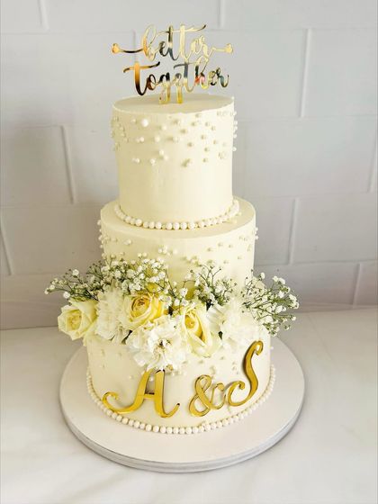 A classic and timeless three-tier wedding cake. The simple pearl detailing and arrangement of fresh baby's breath and yellow roses create a look of pure elegance.