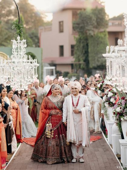 The couple's grand procession down the aisle, lined with guests and crystal chandeliers, showcasing the scale of the celebration.