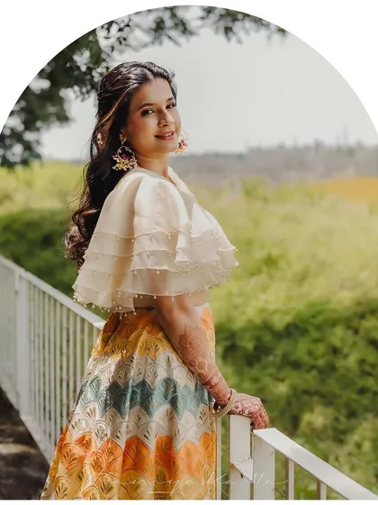 A portrait of a happy client in her custom chevron-patterned lehenga. The organza cape-style blouse with pearl detailing adds a modern and playful touch to this pre-wedding outfit.