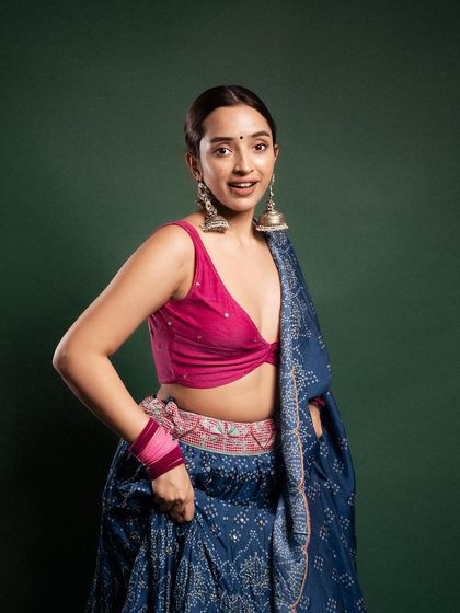 A bright and cheerful portrait for a festive collection. The combination of a pink blouse and blue lehenga, along with the model's engaging smile, creates a welcoming and vibrant image.