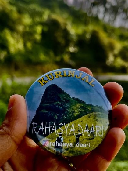 A beautifully lit shot of the Kurinjal trek badge, with the green hills in the background.