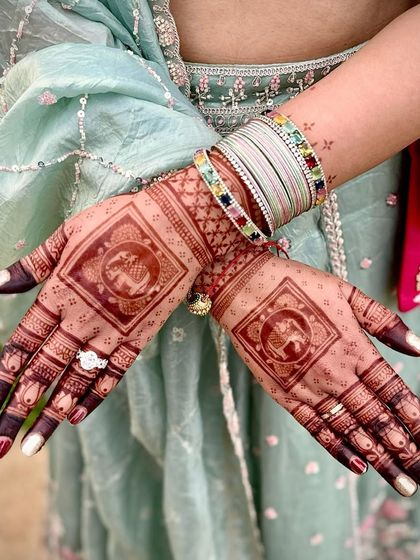 This design features a central square element with a traditional elephant motif, a symbol of good luck and prosperity. The fingers are tipped with dark henna for a classic bridal look.