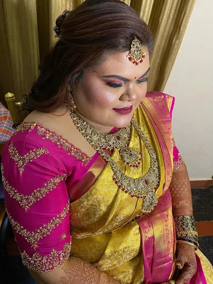 A glamorous reception look. The bride's yellow and pink saree is paired with a soft, open hairstyle, perfect for an evening of celebration.