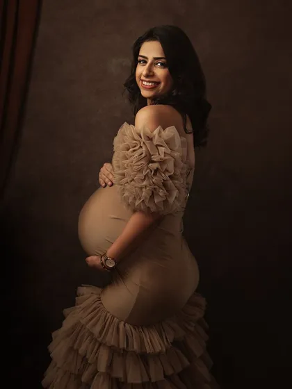 A radiant smile from the mother-to-be. The ruffled gown adds a touch of glamour and softness, perfectly complementing her joyful expression.