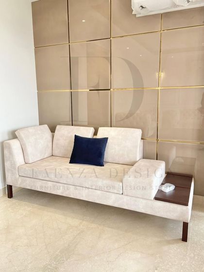 This custom daybed, featuring an integrated wooden side table, is perfect for a cozy reading nook or a guest seating area. The beige upholstery and clean lines complement the lacquered, gold-inlaid wall panels behind it.