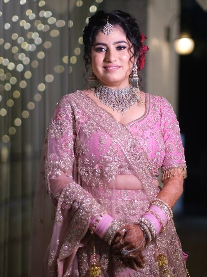 A radiant bridal portrait. The bride's happy expression and beautiful pink lehenga are perfectly illuminated against a backdrop of twinkling lights.