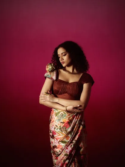 This look features natural curls and soft, earthy makeup tones that complement the printed saree and fringed blouse, creating a cohesive, bohemian-inspired fashion look.
