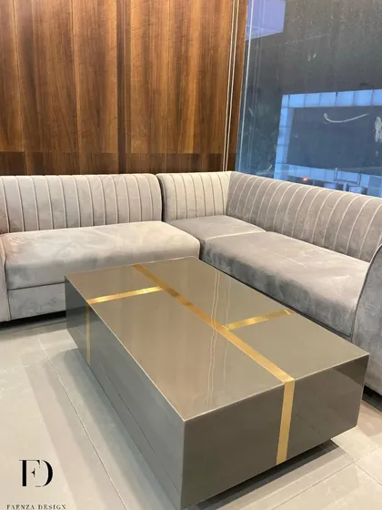 A grey L-shaped sectional with a low back and deep seats. The design is paired with a center table featuring a high-gloss finish and brass inlay, creating a sleek and modern entertainment space.