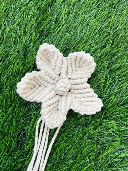 A single, beautifully crafted macrame flower in a natural, off-white color. These can be used as decorative accents, gift toppers, or part of a larger floral arrangement.