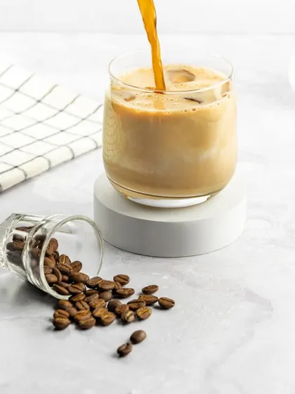 This image captures the beautiful moment when milk is added to iced coffee. The clean, bright background keeps the focus on the drink itself, highlighting the creamy texture and refreshing look.