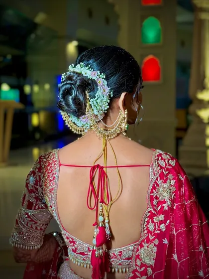 An elegant and clean bridal bun, beautifully decorated with a semi-circle of fresh baby's breath and other delicate flowers. This updo is perfect for securing a dupatta and provides a classic, polished look for the wedding pheras.
