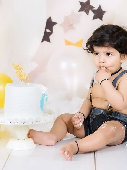 A thoughtful moment during a cake smash, as the baby boy curiously tastes the frosting from his finger.