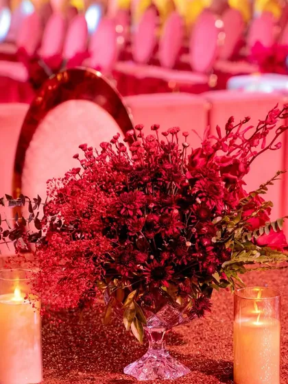 A close-up of a centerpiece with deep red flowers and candles, showcasing the rich textures and colors that defined the event's decor.