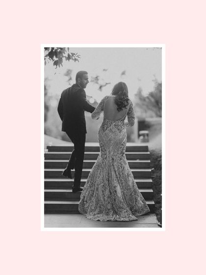 A timeless black and white shot of the couple walking up the stairs. The focus on the back of Jahanvi's stunning gown and John leading her by the hand creates a classic, romantic narrative.