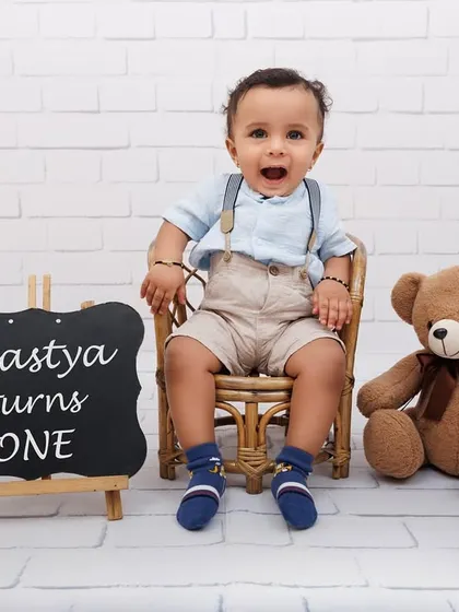 A happy portrait of Agastya celebrating his first birthday with a teddy bear and a personalized sign.