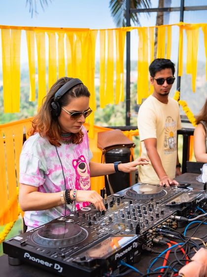 A DJ spins tracks at our Goa Holi party, set against a backdrop of festive yellow decor. I curate the music to match the high-energy, sun-soaked vibe of a daytime beachside celebration.