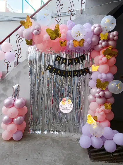 A pastel pink and purple butterfly-themed balloon arch with a silver shimmer curtain.