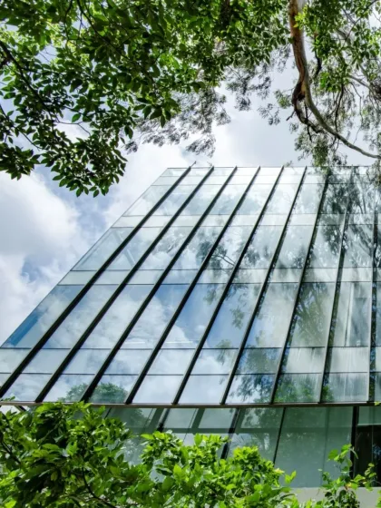 Where architecture meets nature’s poetry. The angled glass facade of this building reflects the sky and is framed by lush greenery, showcasing our biophilic design principles.