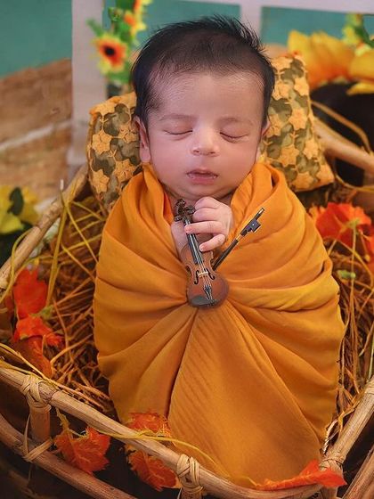 A little country man. This baby is swaddled in a warm orange wrap and placed in a rustic basket with sunflowers and vintage lanterns. It’s a cozy, rustic theme perfect for a baby boy.