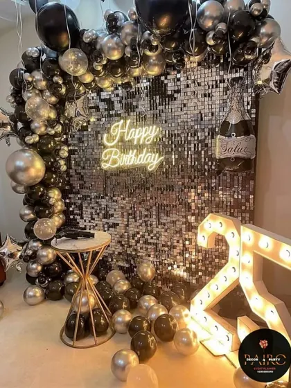 A sophisticated setup for a 25th birthday, featuring a silver sequin wall, a black and silver balloon arch, and marquee numbers.