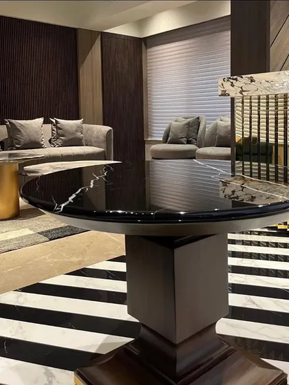 This perspective emphasizes the layered design of the Juhu living space. The foreground features a striking black marble table, leading the eye towards the comfortable seating area and textured walls beyond.