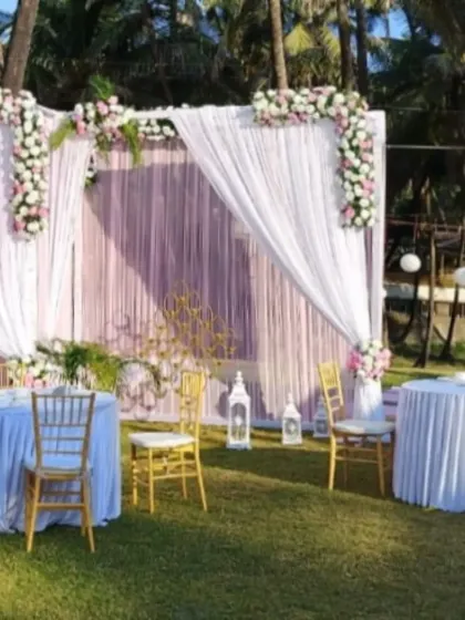 A simple and elegant decor setup for a destination wedding on a lawn, featuring a white and lavender drape backdrop and guest seating.