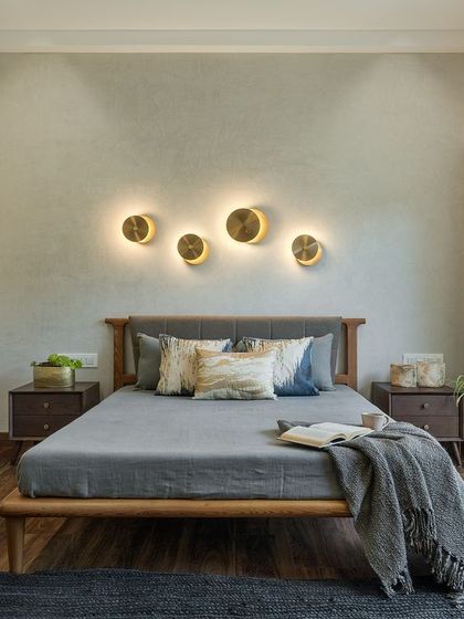 In this master bedroom design, I used unique, back-lit wall sconces that resemble celestial bodies to create a focal point above the bed. The combination of a textured grey wall, fluted wardrobe panels, and warm wood flooring results in a sophisticated and serene atmosphere.