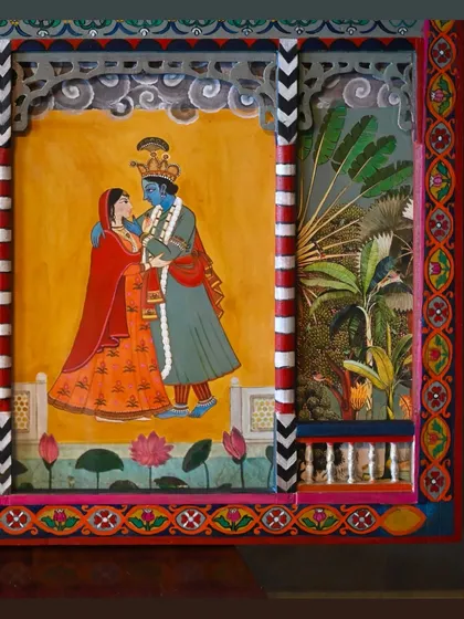 A close-up of the second portrait of Radha and Krishna, now set within the restored and painted panel. The surrounding details, from the painted pillars to the tropical foliage, create a complete scene.