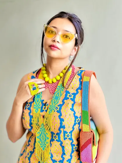 A portrait shot showing the layered necklaces and colorful bag. The yellow-tinted glasses add to the Y2K, hippie aesthetic.