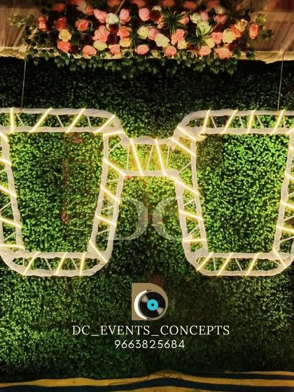 A fun and quirky selfie booth created for a party, featuring a green hedge wall and oversized, illuminated sunglasses for a unique photo opportunity.