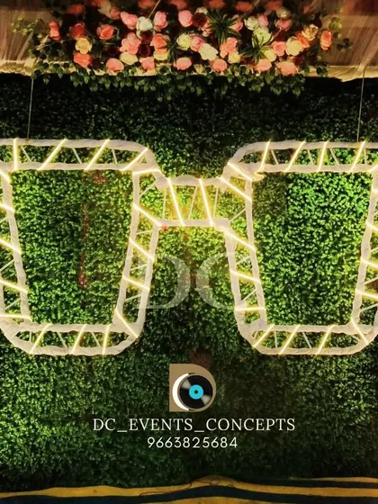 A fun and quirky selfie booth created for a party, featuring a green hedge wall and oversized, illuminated sunglasses for a unique photo opportunity.