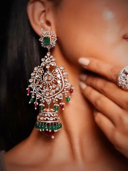 The art of tradition, redefined for the modern bride. These magnificent chandelier earrings showcase intricate Polki work, accented with precious emeralds and rubies, and finished with delicate pearl drops. Each element is meticulously handcrafted to create a wearable piece of heritage.