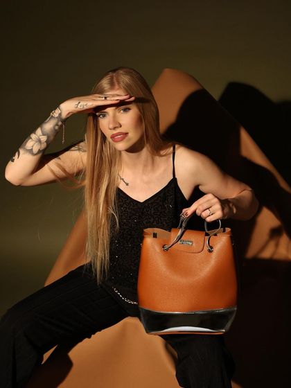 In this editorial-style shoot, I used dramatic lighting and a unique pose to create a sense of adventure and style. The model's gaze and the rich, earthy tones of the backdrop complement the tan leather handbag.