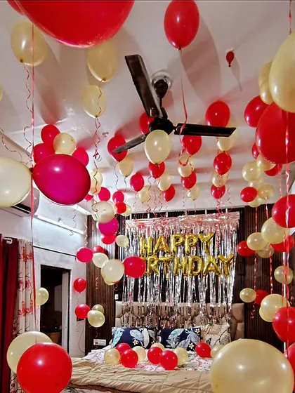 A romantic bedroom decoration with red and cream balloons covering the ceiling and a "Happy Birthday" foil banner over the bed.