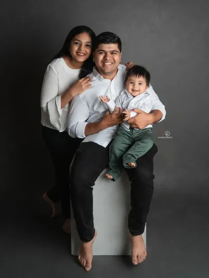 A happy family of three. This classic studio portrait with a simple grey backdrop is all about capturing the smiles and connection between the parents and their baby boy.