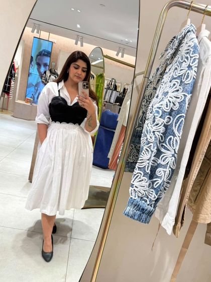 A classic white shirt and skirt get a modern edge by layering a black corset over them. This creates a powerful, structured look from three simple pieces.