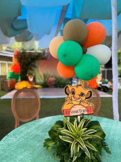 A close up of a table centerpiece for a Lion King themed first birthday. Each table featured a unique arrangement with lush greenery, a character cutout of young Simba, and a balloon cluster in safari colors.