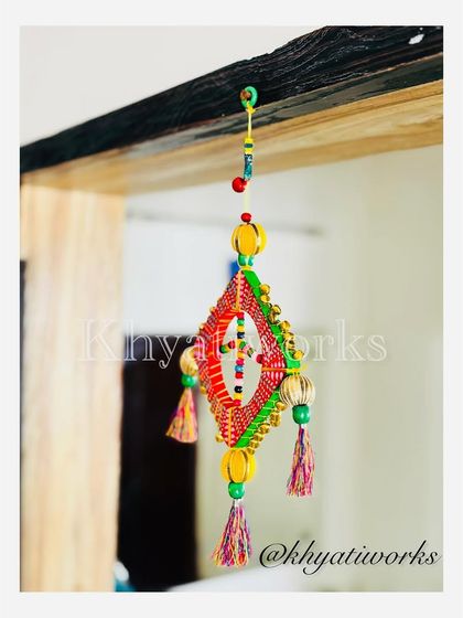 My kite-themed wall art hanging from a wooden beam. The bright red and green colors, along with the colorful tassels, make it a joyful addition to any space.