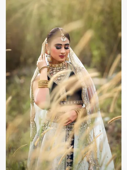 An outdoor bridal shoot capturing a serene and elegant moment. The natural setting complements the traditional lehenga, and the soft lighting highlights the delicate details of the fabric and embroidery.