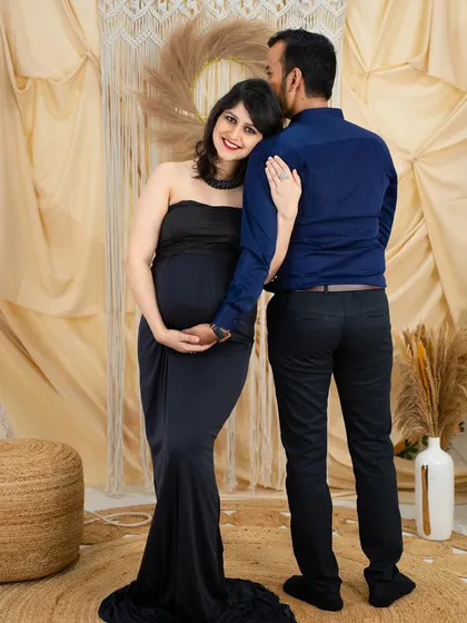 A sweet and loving couple's portrait. The partner kisses the mom-to-be's head from behind as she leans back into his embrace, both smiling.