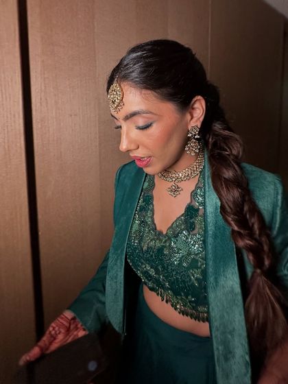 The bride is ready for her Sangeet in a beautiful green outfit, her hair styled in a modern and chic fishtail braid.