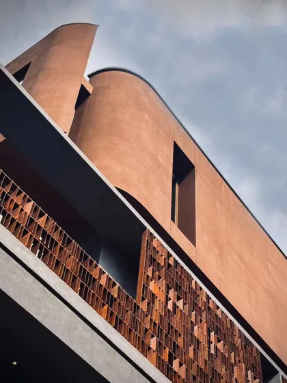 A detail of the façade reveals the rhythmic interplay between the warm, textured terracotta screen and the monolithic, curved structure. This juxtaposition of materials and a focus on refined detailing are central to our architectural language.