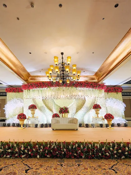 We specialize in creating opulent reception stages that serve as the magnificent centerpiece of your celebration. This design features a grand floral canopy of red and white roses with cascading crystal elements.