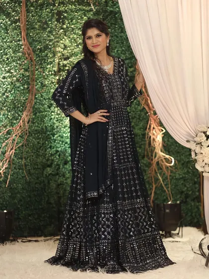 A full-length view of a stunning navy blue Anarkali look. The makeup is kept elegant and subtle to balance the heavily embellished outfit, with a focus on flawless skin and soft hair.