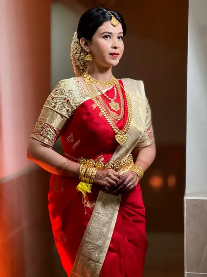 A full-length portrait of bride Srishti. The classic red and cream combination of her silk saree is a timeless choice for a Kerala bride.