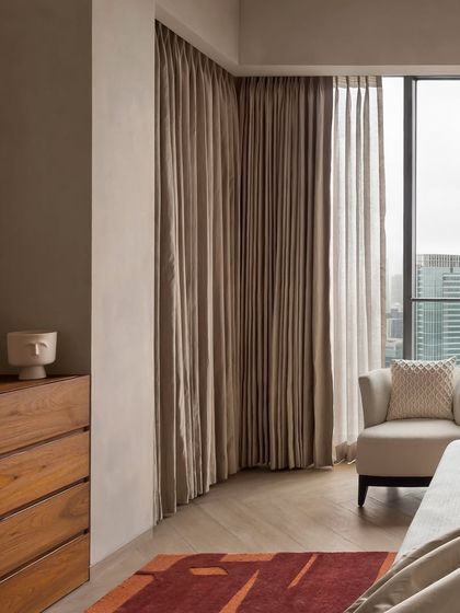 This corner of the East Coast Residence bedroom shows the simple, elegant lines of the wooden dresser and the soft, floor-to-ceiling curtains that frame the city view.